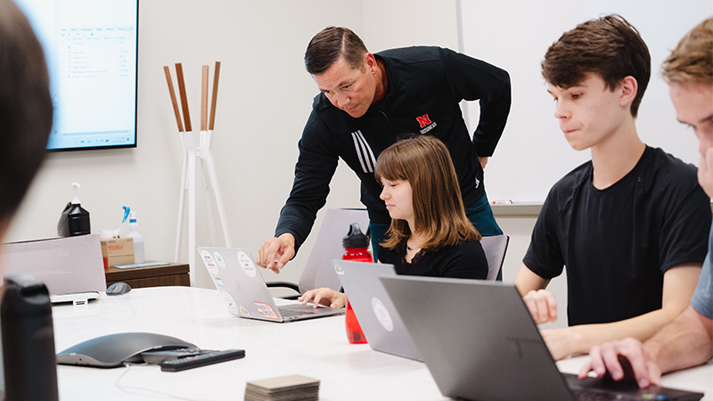 A group collaborating at a table with laptops in a bright office setting.