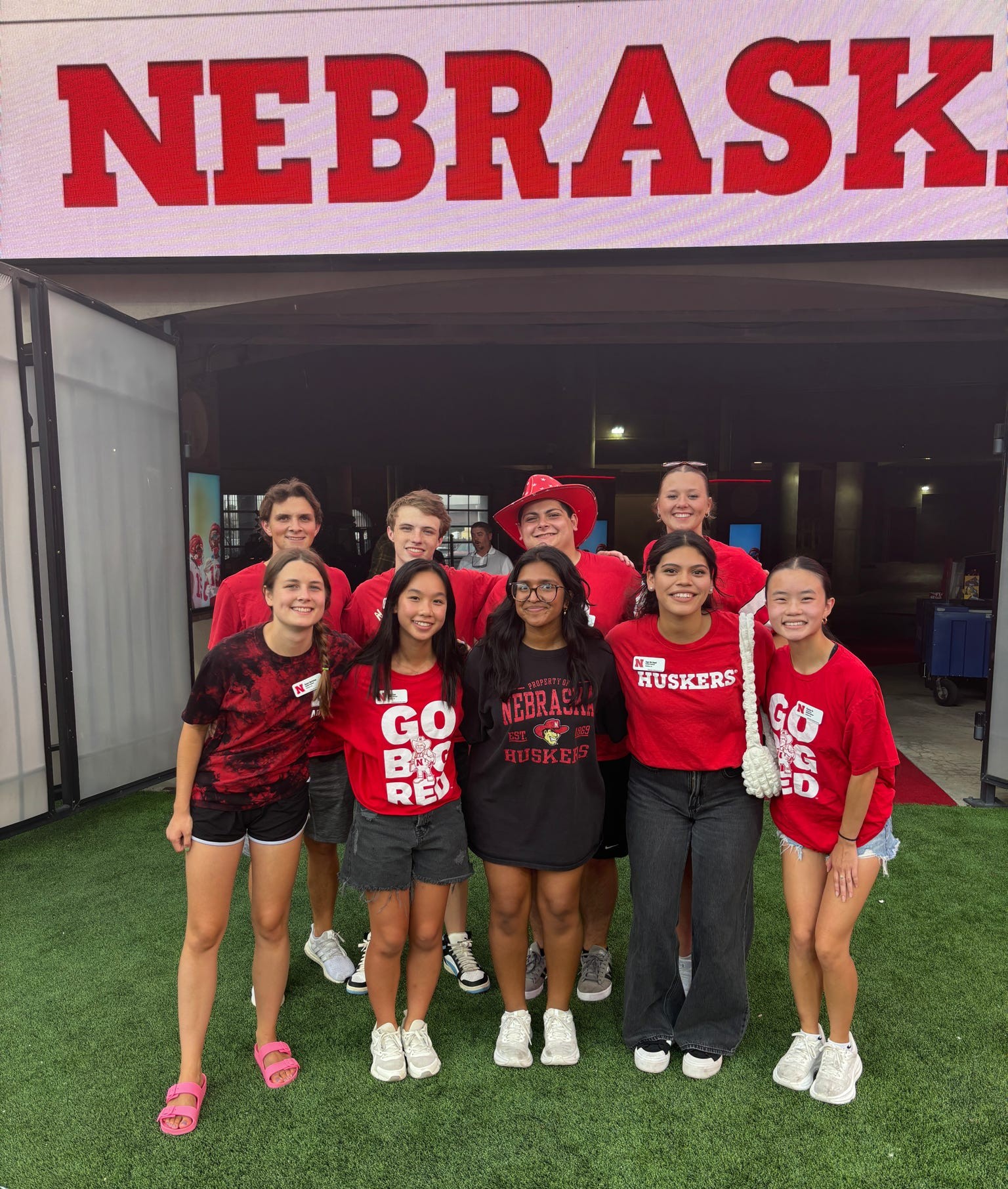 Subedi with group of smiling people wearing red and black clothing in front of a Nebraska sign outdoors.