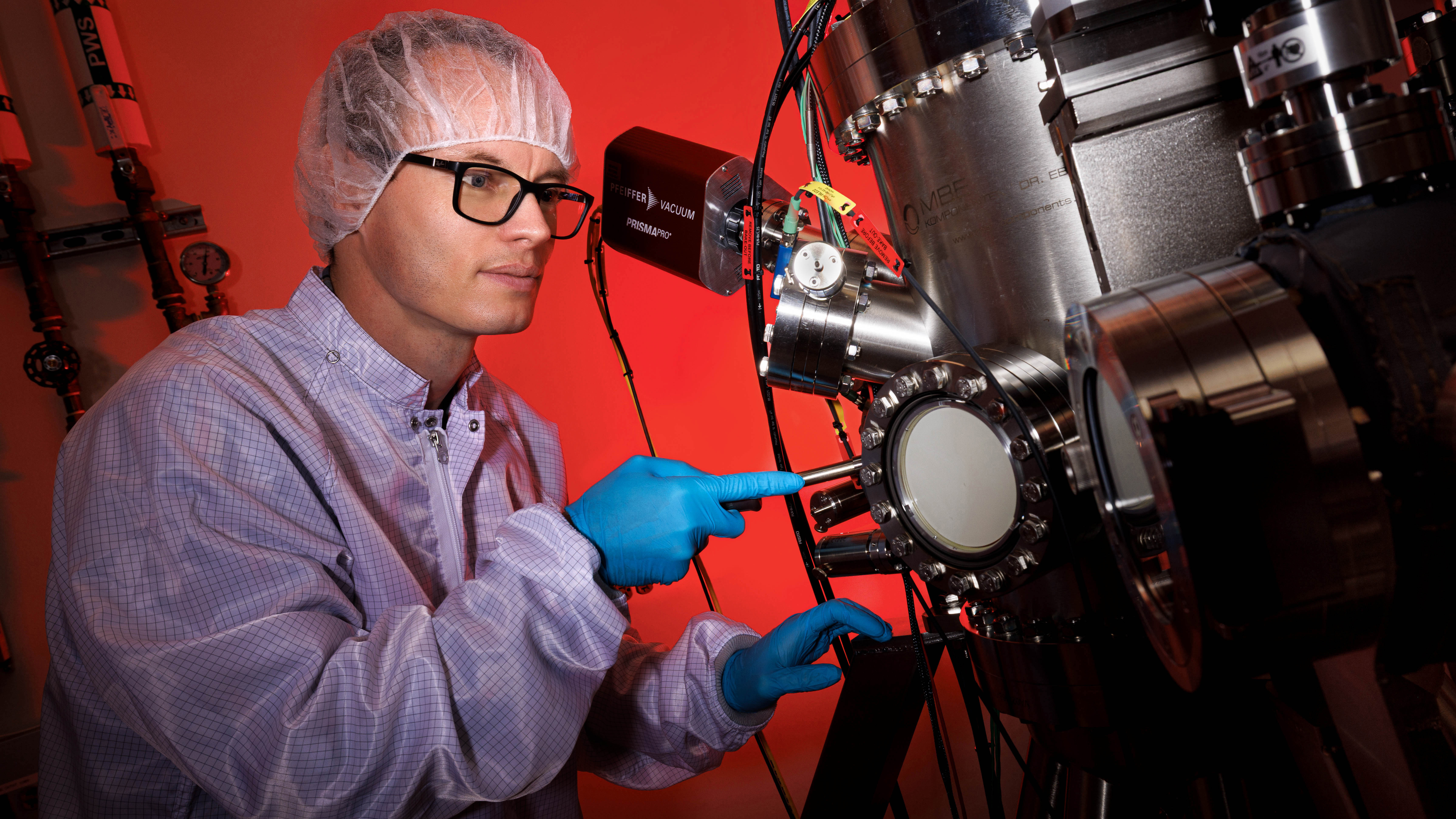 Robert Streubel, assistant professor of physics and astronomy at the University of Nebraska–Lincoln, wears gloves and a hairnet as he uses a large metal machine in his lab.