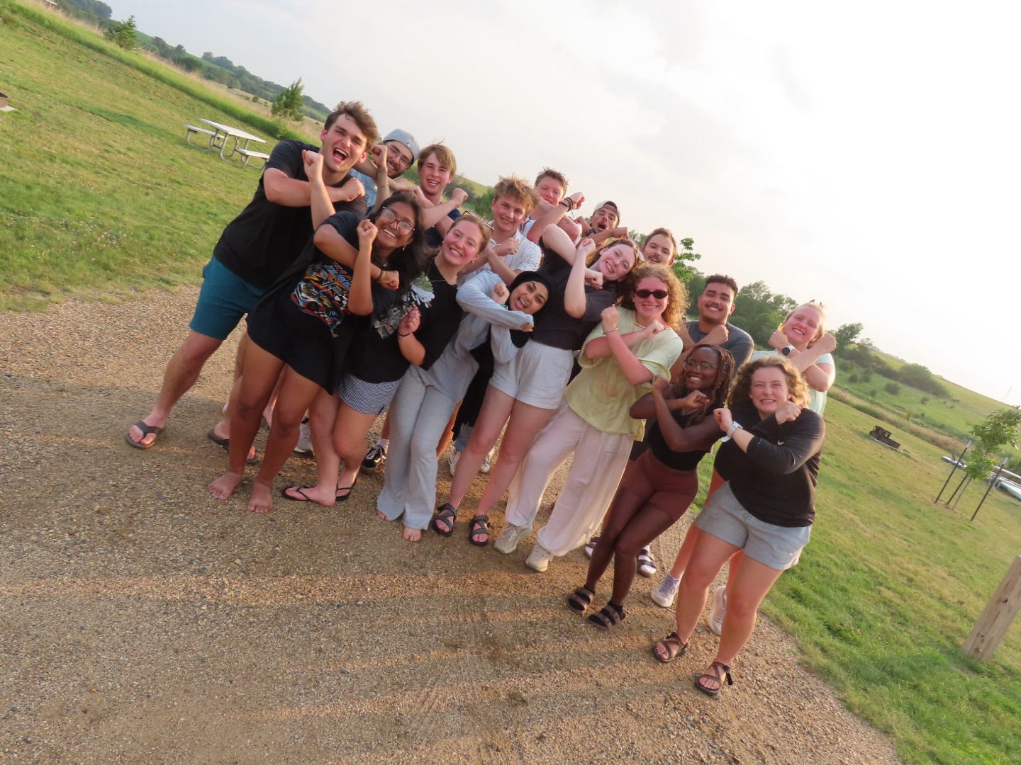 Group of people smiling and posing outdoors, crossing their arms in an open grassy area.