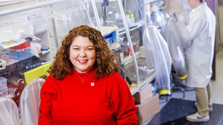 Dr. Nicole Buan sits on the left side of the frame in a red sweater, in front of a lab.