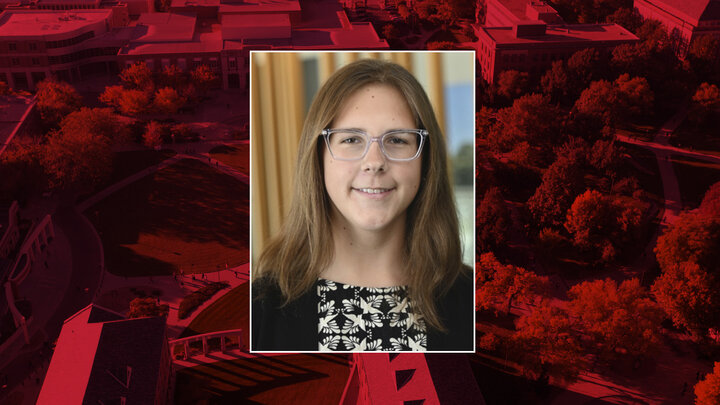 Abby Veiman is photographed wearing a black blazer over a black and white patterned shirt, surrounded by a red background.