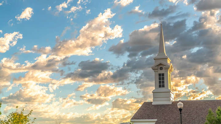 A church steeple rises up to clouds in yellows and golds from sunlight.