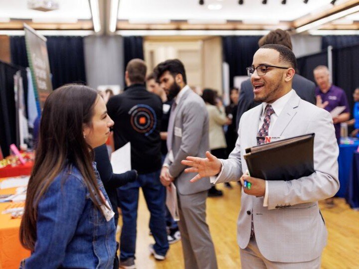 Professional networking event with people conversing and booths in a bright conference room.