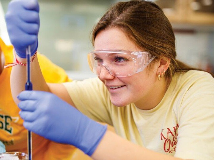 Person in gloves using a pipette in a lab setting.