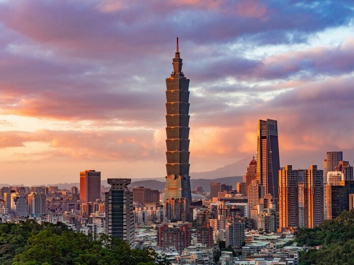 Taipei skyline at sunset, featuring Taipei 101 and scattered buildings surrounded by greenery.